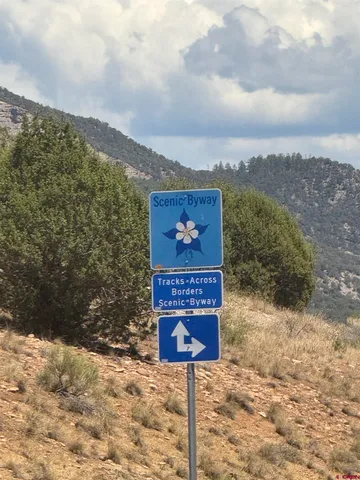 a sign board with road and tall buildings in the background