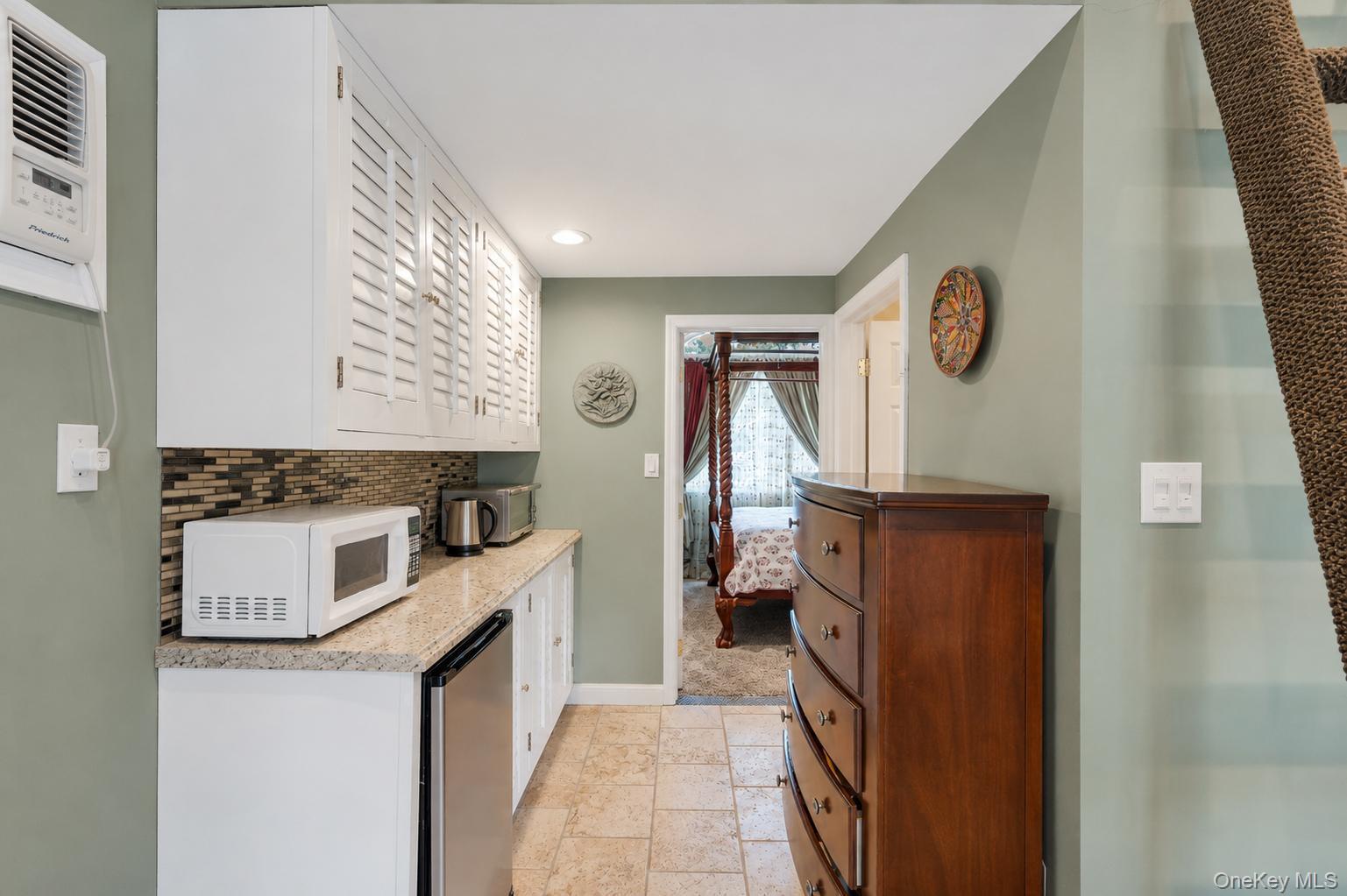 19 Joan Road Bay Shore, NY 11706 - Photo 35 of 50 Galley area featuring white shaker-style cabinetry with louvered doors, a mosaic tile backsplash, and a granite-finish countertop