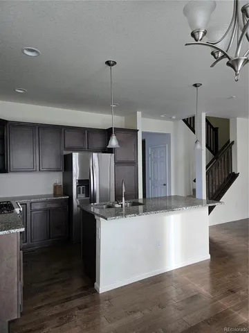 a kitchen with stainless steel appliances kitchen island granite countertop a refrigerator a stove and a sink with wooden floor