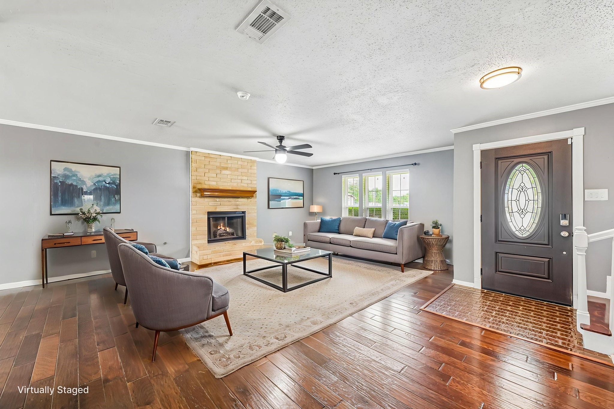 8 Arlington Street Conroe, TX 77301 - Photo 2 of 37 This inviting living room features hardwood floors, a cozy brick fireplace, and large windows providing natural light. It is tastefully staged with modern furniture, including a comfortable sofa, armchairs, and a sleek coffee table. The elegant front door adds a welcoming touch.