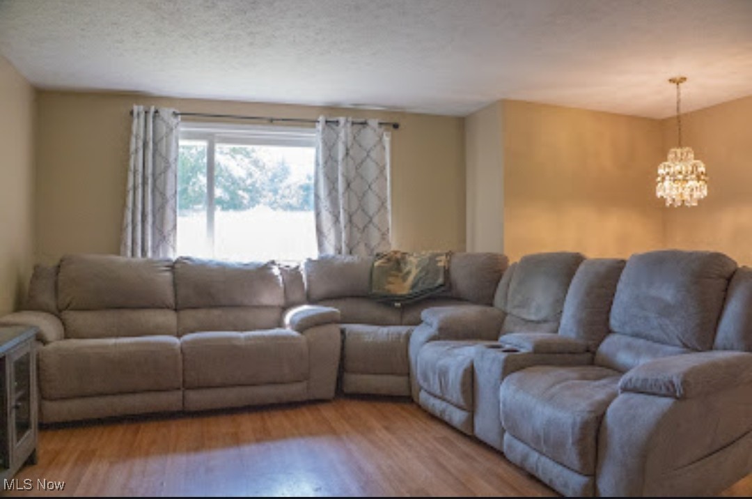 1770 Meadows Road Madison, OH 44057 - Photo 6 of 22 Living room featuring a chandelier, light wood finished floors, and a textured ceiling