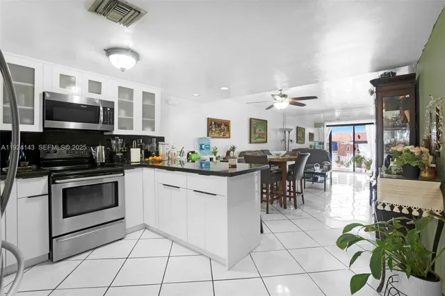 a kitchen with stainless steel appliances granite countertop a stove top oven a sink a dining table and chairs with white cabinets