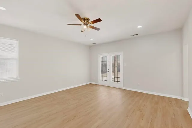 an empty room with wooden floor fan and windows