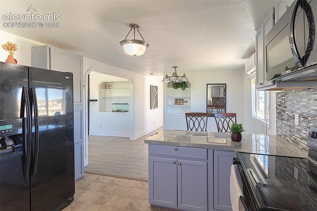 3425-3435 Wiesner Road Calhan, CO 80808 - Photo 10 of 25 Kitchen featuring black appliances, tile counters, a peninsula, built in features, and a textured ceiling