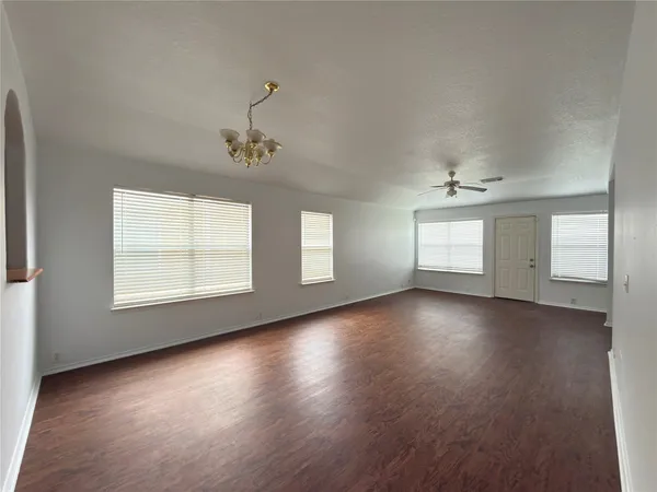 an empty room with wooden floor chandelier and windows