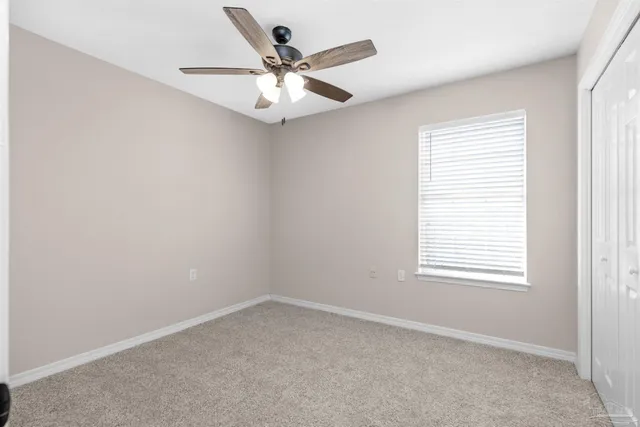 an empty room with chandelier fan and windows