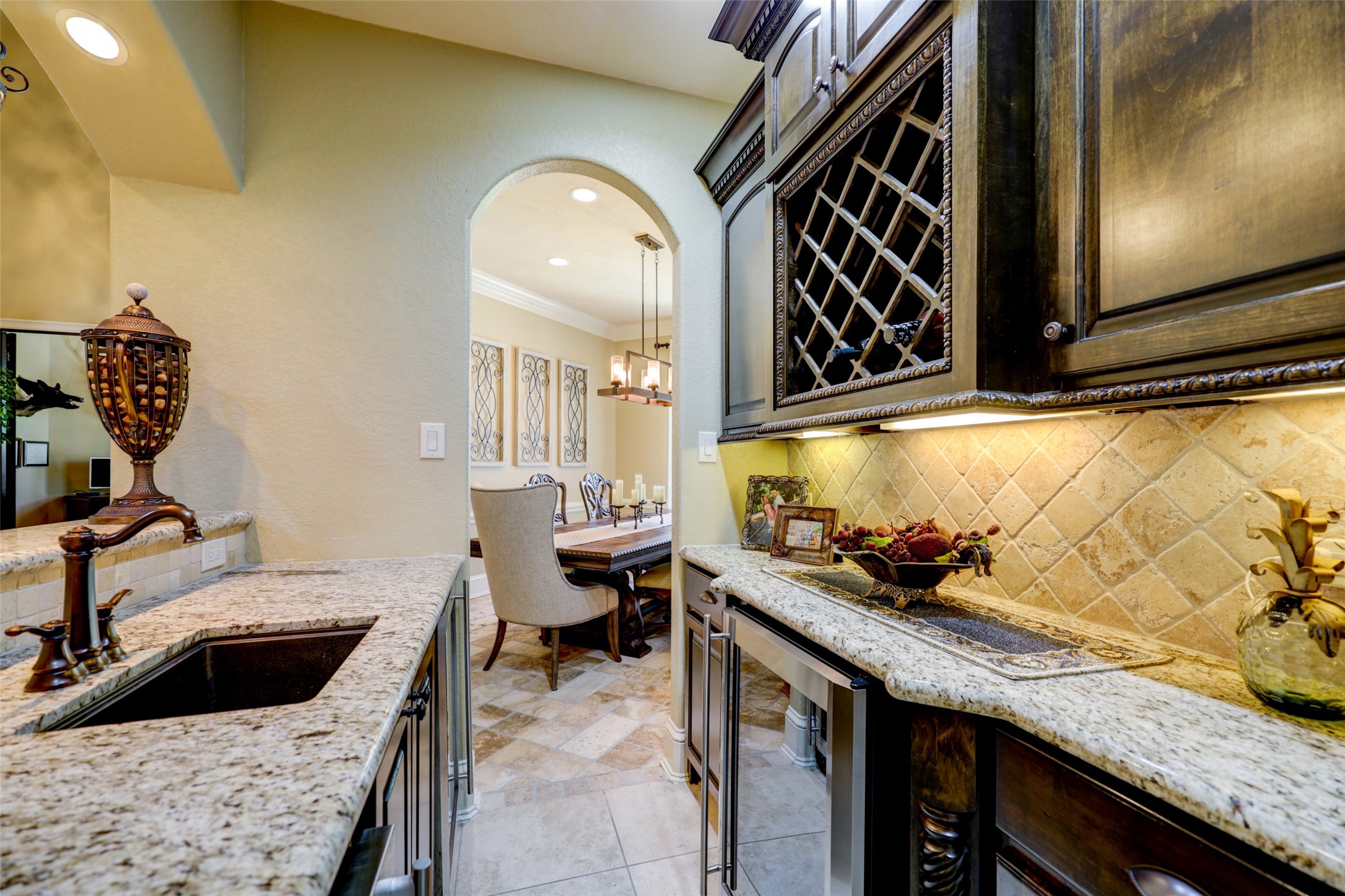 4434 Chateau Creek Way Spring, TX 77386 - Photo 13 of 34 This photo showcases an elegant butler's pantry with granite countertops, rich dark wood cabinetry, and a wine rack. It opens into a dining area with stylish decor and warm lighting, creating a seamless transition for entertaining.