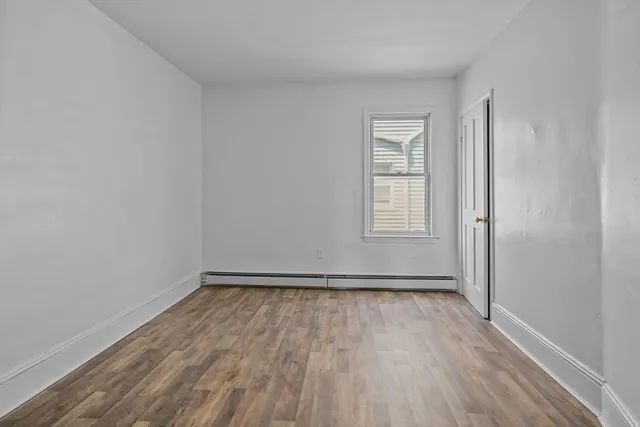 a view of an empty room with wooden floor and window
