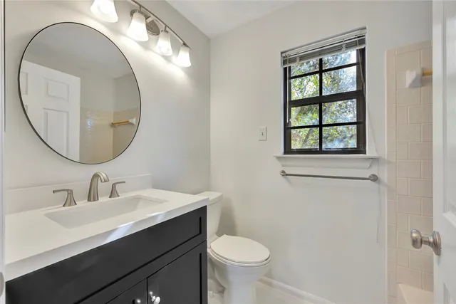 a bathroom with a sink a mirror a toilet and a window