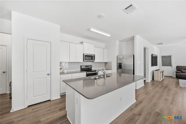 a kitchen with stainless steel appliances granite countertop a refrigerator a sink dishwasher a stove and white countertops with wooden floor