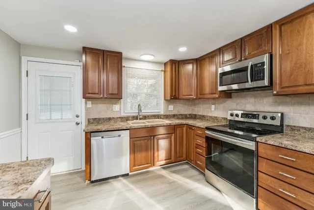 a kitchen with stainless steel appliances granite countertop wooden cabinets a stove a sink and a microwave