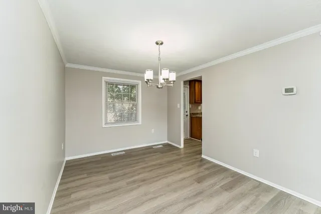 an empty room with wooden floor chandelier and windows