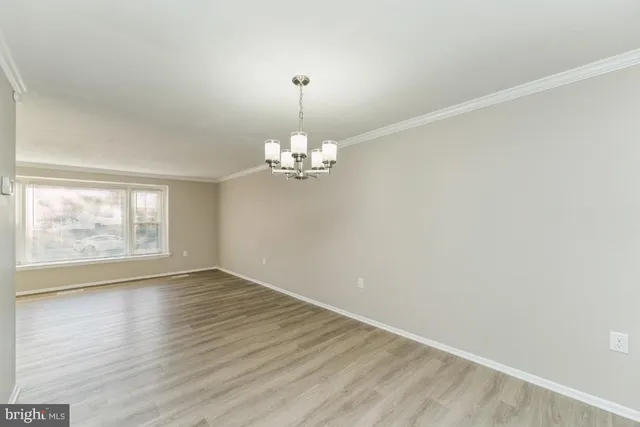 an empty room with wooden floor chandelier and windows