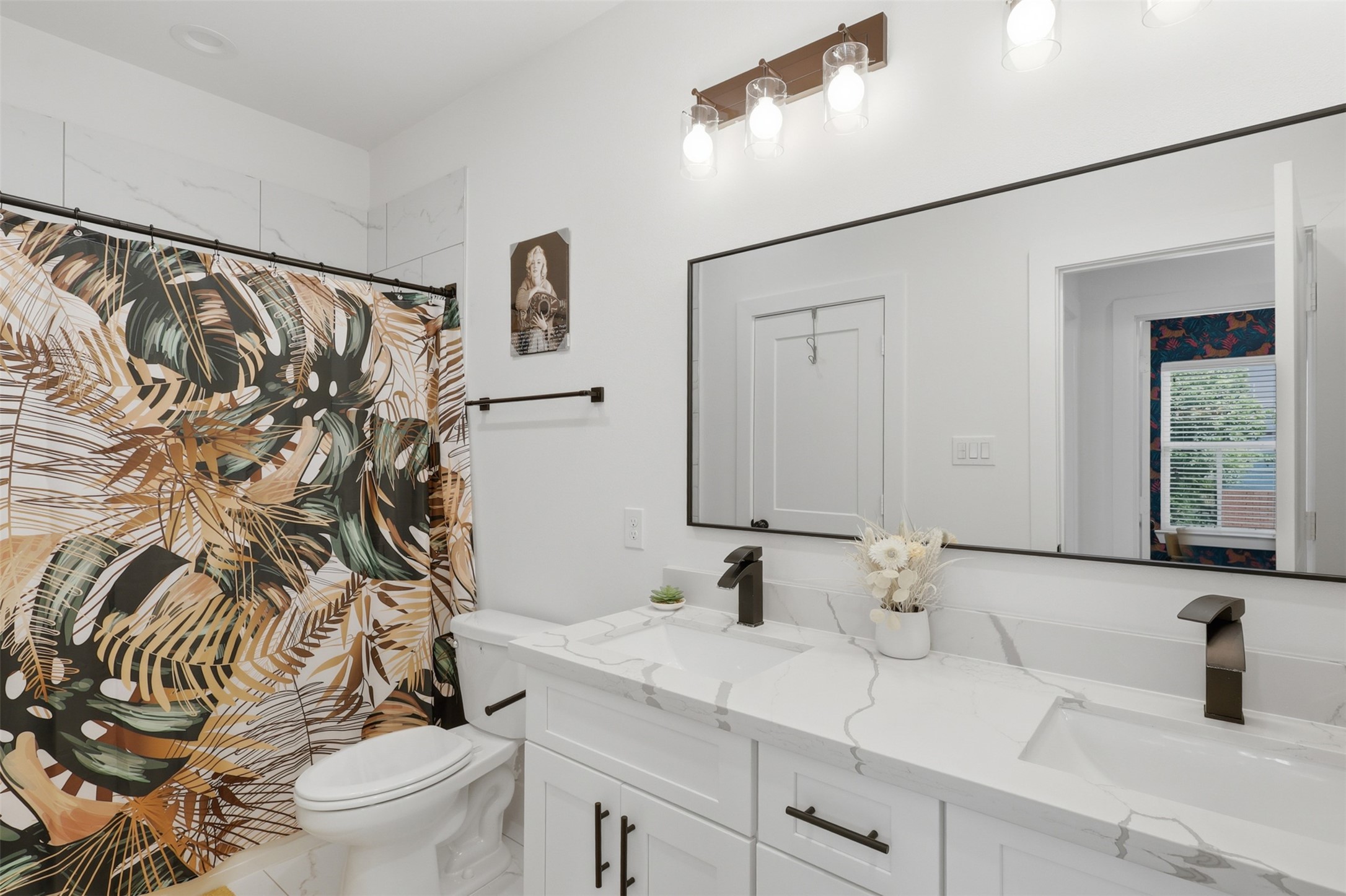 6833 Paris Street Houston, TX 77021 - Photo 17 of 23 This bathroom features a modern design with white cabinetry and a spacious double vanity. The large mirror enhances the space, while the tropical shower curtain adds a vibrant touch. Bright lighting and sleek fixtures complete this stylish, functional area.