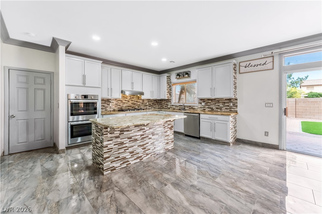 418 Finch Ridge Avenue North Las Vegas, NV 89032 - Photo 15 of 43 Kitchen featuring light stone counters, stainless steel appliances, a kitchen island, tasteful backsplash, and white cabinetry