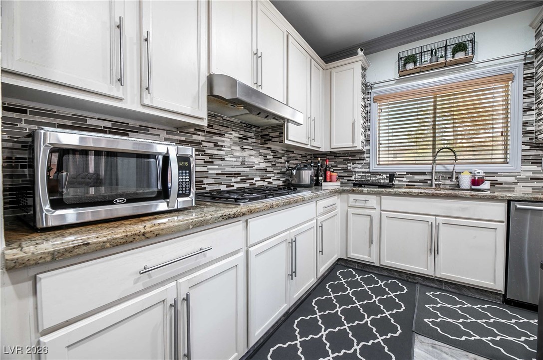 418 Finch Ridge Avenue North Las Vegas, NV 89032 - Photo 16 of 38 Kitchen featuring white cabinets, light stone counters, under cabinet range hood, and crown molding