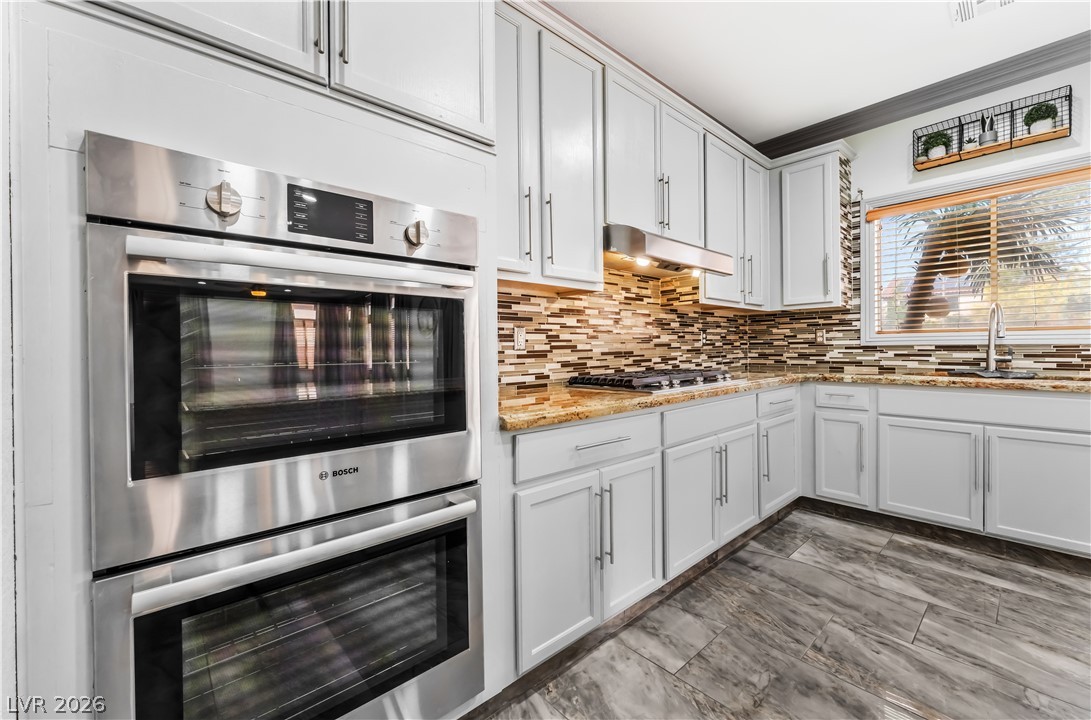 418 Finch Ridge Avenue North Las Vegas, NV 89032 - Photo 19 of 43 Kitchen with stainless steel appliances, white cabinets, ornamental molding, light stone countertops, and decorative backsplash
