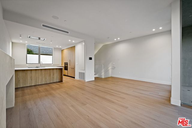 a view of an empty room with wooden floor and a kitchen
