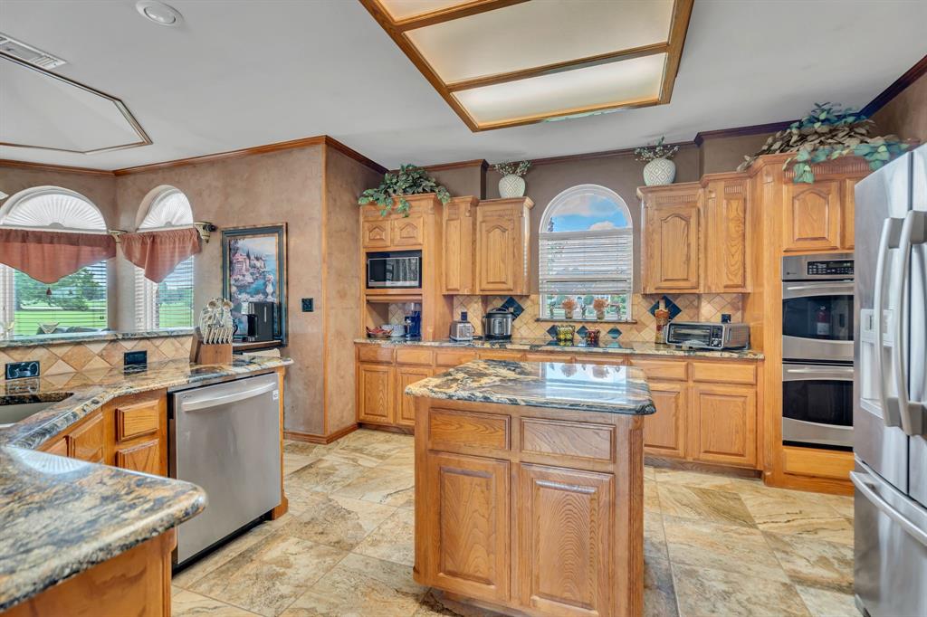 50 Buckingham Lane Allen, TX 75002 - Photo 19 of 39 Kitchen with stone tile flooring, ornamental molding, appliances with stainless steel finishes, tasteful backsplash, and a center island