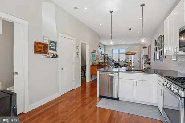 a kitchen with stainless steel appliances granite countertop a refrigerator a sink dishwasher a stove and white cabinets with wooden floor