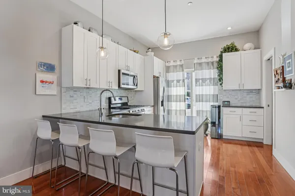 a kitchen with stainless steel appliances granite countertop a stove top oven a refrigerator a sink and white cabinets with wooden floor