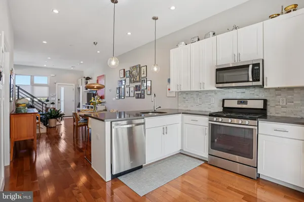 a kitchen with stainless steel appliances granite countertop a stove top oven a sink dishwasher a refrigerator and a dining table with wooden floor
