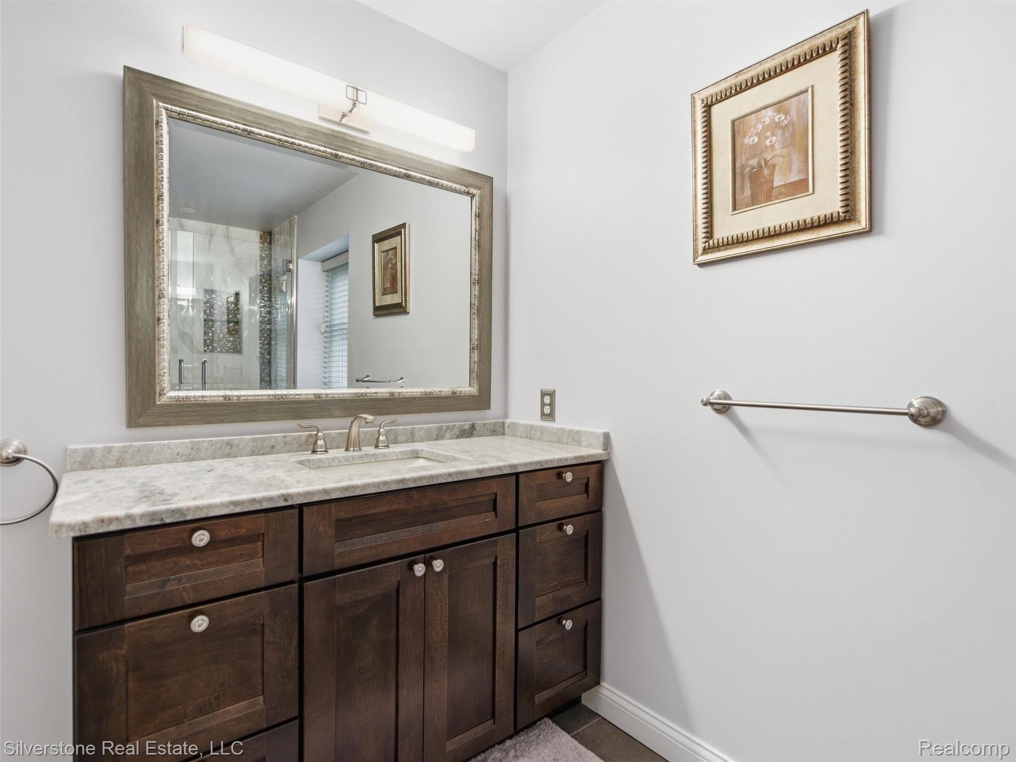 6577 Edith Court Troy, MI 48085 - Photo 42 of 61 Bathroom vanity featuring dark wood cabinetry, a light-toned countertop, and an undermount sink with a brushed nickel faucet