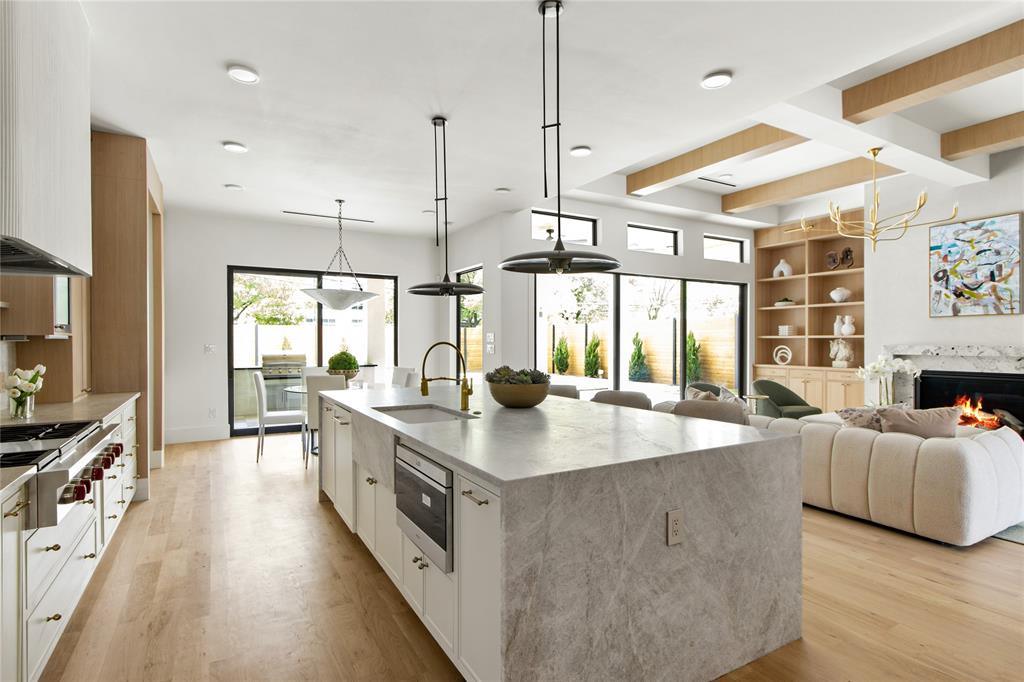 11736 Jamestown Road Dallas, TX 75230 - Photo 1 of 1 Kitchen with stainless steel gas stovetop, a large island with sink, a sink, light wood-style flooring, and white cabinetry