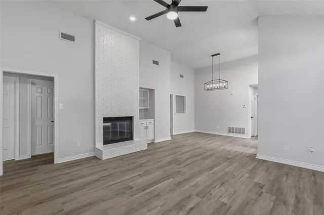an empty room with wooden floor a ceiling fan a fireplace and windows