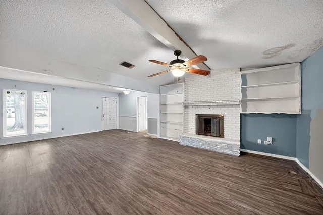 a view of an empty room with wooden floor fireplace and a window