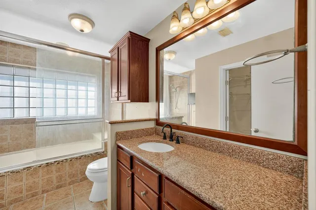 a bathroom with a granite countertop sink a toilet a mirror and bathtub