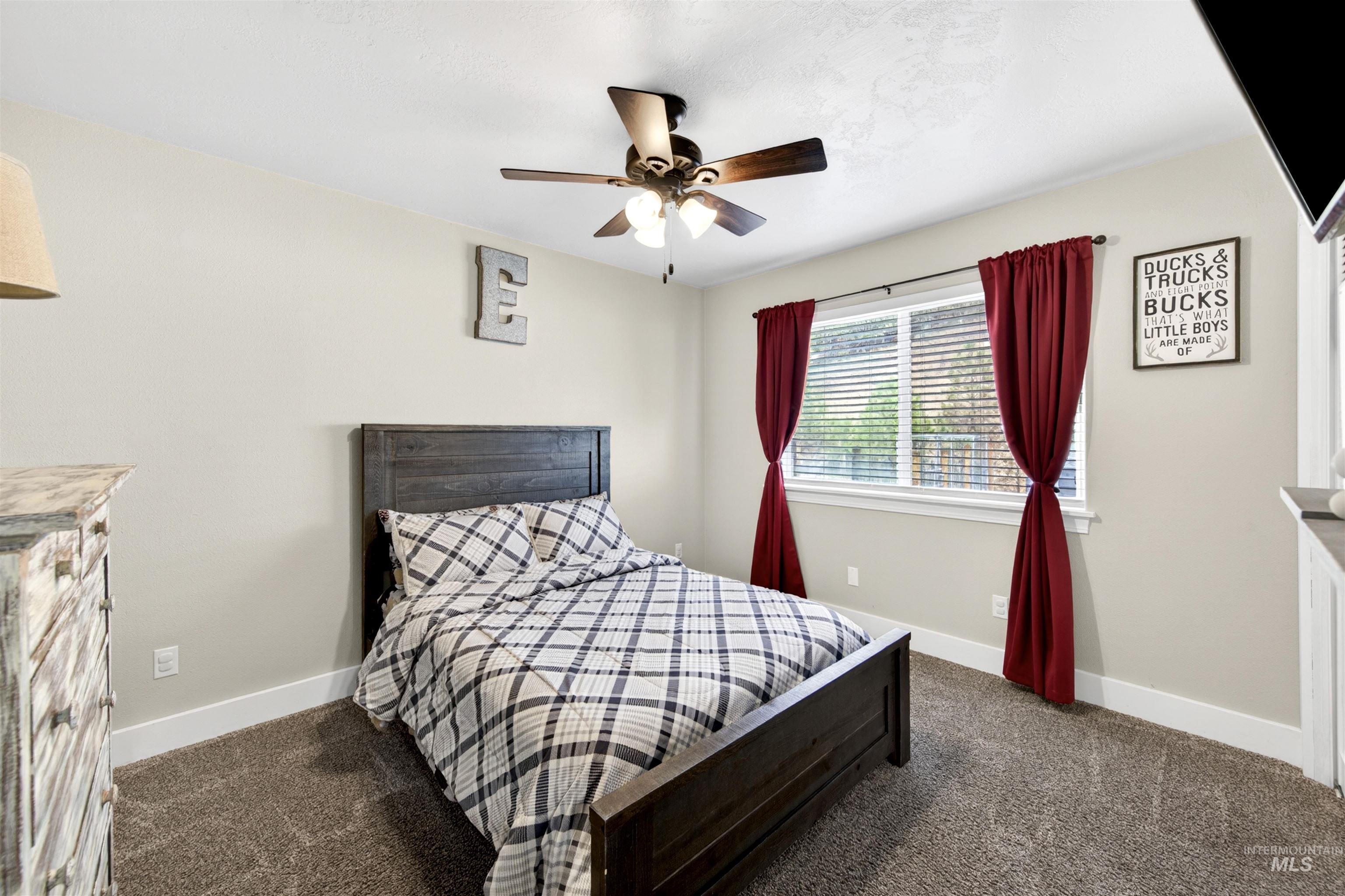 4 Round Up Circle Boise, ID 83716 - Photo 32 of 47 Neutral wall paint, plush carpet flooring, a window with blinds and drapes, a ceiling fan with integrated lighting, and white baseboards