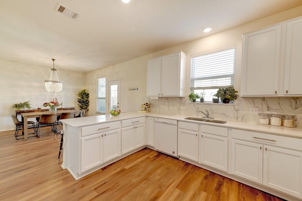 13916 Inaugural Street Manor, TX 78653 - Photo 15 of 28 Bright hardwood flooring complements the pristine white cabinetry and marble backsplash in this inviting kitchen and dining area.