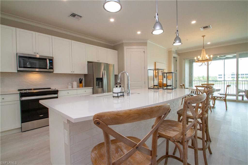 251 Indies Drive East, Unit 202 Naples, FL 34114 - Photo 10 of 48 a kitchen with stainless steel appliances kitchen island granite countertop a stove a sink a dining table and chairs