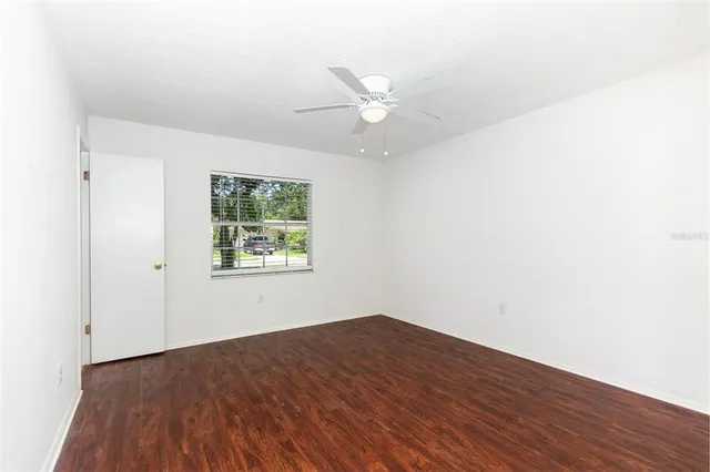 an empty room with wooden floor window and ceiling fan