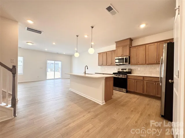 a large kitchen with stainless steel appliances kitchen island granite countertop a stove a sink a refrigerator and white cabinets with wooden floor
