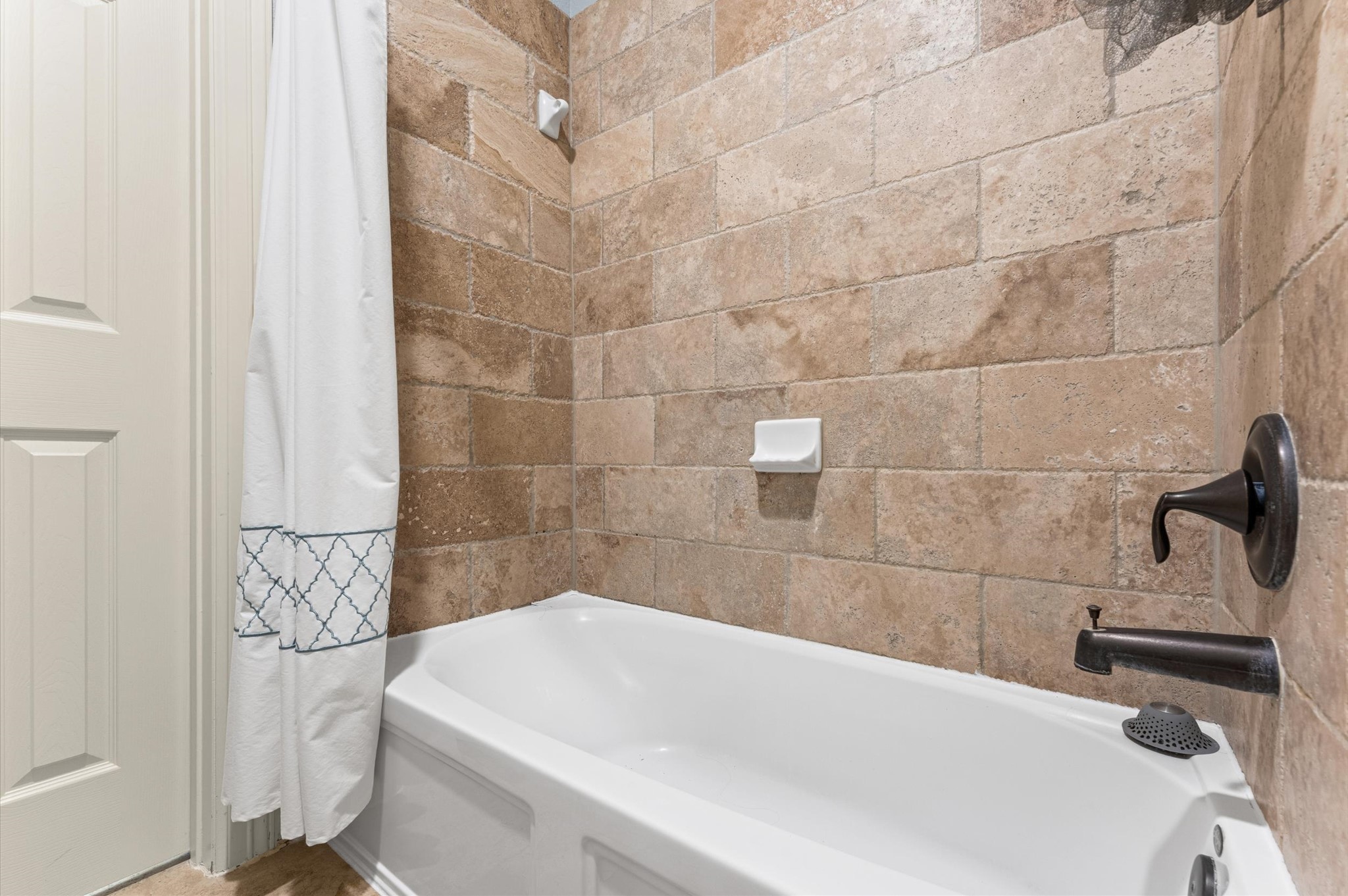 70 Valera Ridge Drive Spring, TX 77389 - Photo 29 of 37 This bathroom features a traditional bathtub with a tile surround in warm, earthy tones. It includes a dark faucet and a simple, elegant shower curtain.