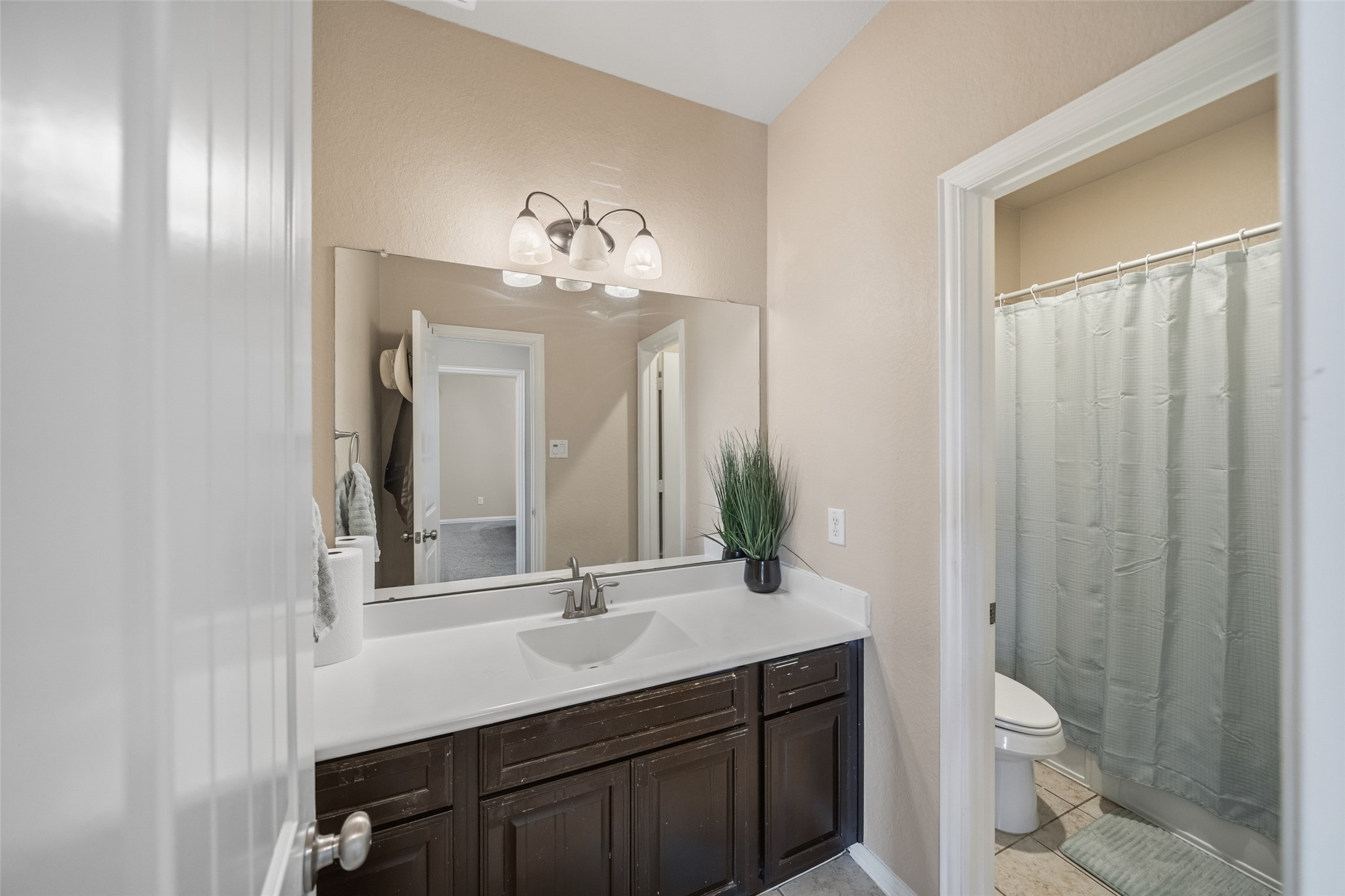 4747 Abercorn Street Rosharon, TX 77583 - Photo 29 of 46 This bathroom features a modern design with a sleek dark wood vanity, a large mirror, and elegant lighting. It includes a shower with a curtain and neutral-toned tiles, creating a clean and inviting space.