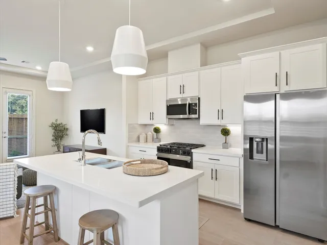 a kitchen with stainless steel appliances kitchen island granite countertop a sink a stove a refrigerator and white cabinets with wooden floor