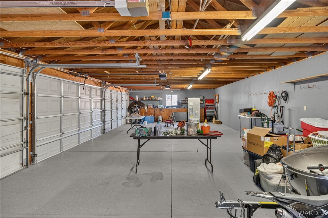 784 Pegasus Ranch Road Bullhead City, AZ 86429 - Photo 60 of 100 Spacious garage featuring a concrete floor, exposed wood beam ceiling, multiple overhead light fixtures, and several roll-up garage doors