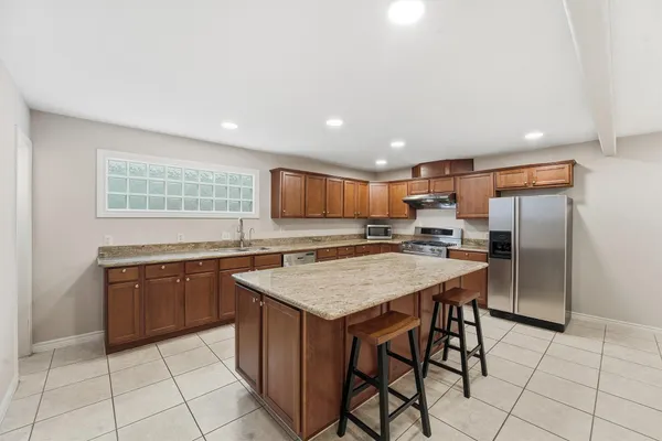 a kitchen with stainless steel appliances granite countertop a refrigerator a sink a stove a dining table and chairs