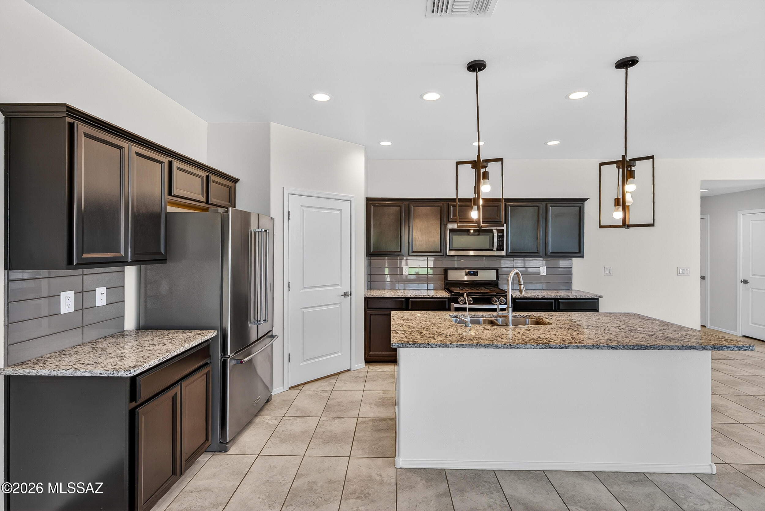 7556 South Circulo Rio Blanco Tucson, AZ 85756 - Photo 8 of 50 Gorgeous chef’s kitchen featuring dark espresso cabinets, granite countertops, a large central island with sink, stainless steel appliances, and pendant lighting. Open layout flows perfectly into the great room and backyard.