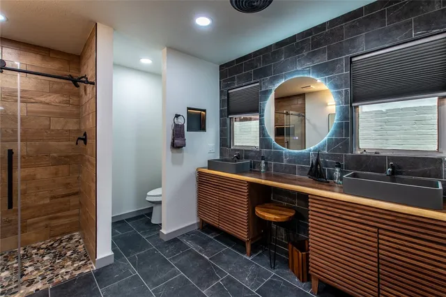 a bathroom with a double vanity sink a toilet a mirror and shower