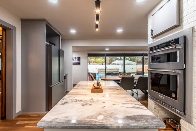 a large kitchen with stainless steel appliances kitchen island granite countertop a refrigerator a stove and a sink with wooden floor