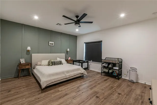 a bedroom with a bed a dresser and potted plants with wooden floor
