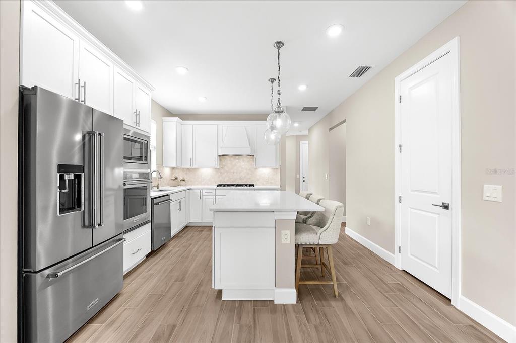 6791 Alstead Circle Lakewood Ranch, FL 34202 - Photo 2 of 25 a kitchen with stainless steel appliances a refrigerator a stove a sink dishwasher and a dining table with wooden floor