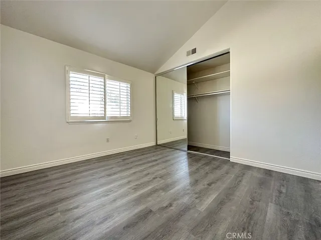 an empty room with wooden floor closet and windows