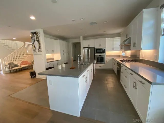 a large kitchen with stainless steel appliances a sink a counter top space cabinets and a couch