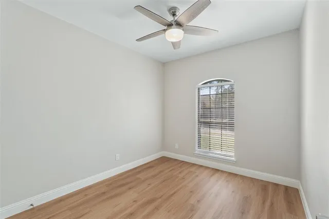 an empty room with wooden floor chandelier fan and windows