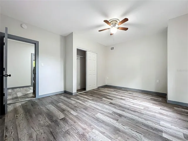 a view of an empty room with wooden floor and a ceiling fan